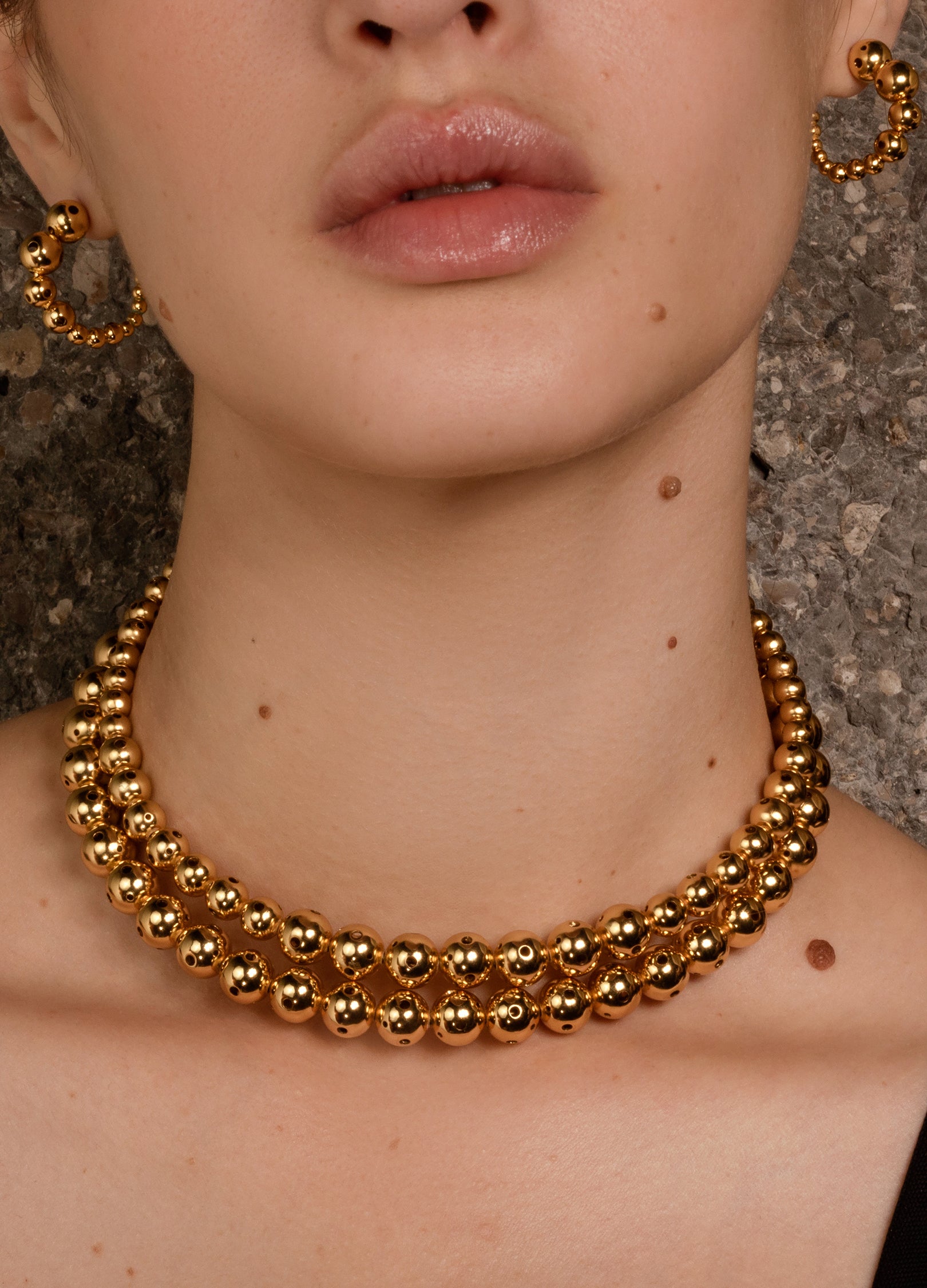 Front close up of a model wearing a gold beaded necklace twisted two times featuring varying sphere sizes. 