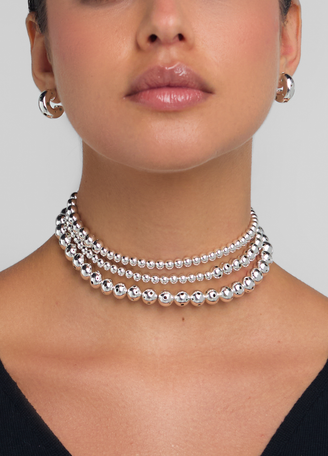 Front close up of a model wearing a silver beaded necklace twisted three times featuring varying sphere sizes. 